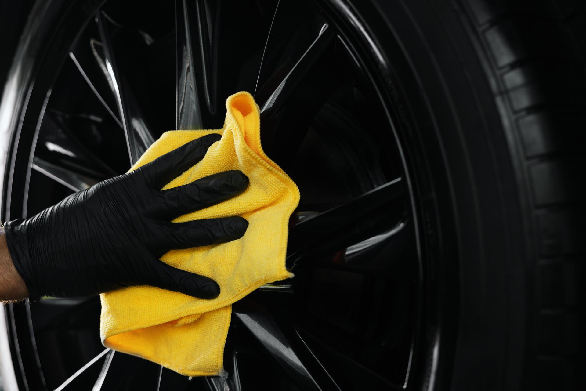 car detailing. hand is cleaning a black alloy wheel with microfiber cloth