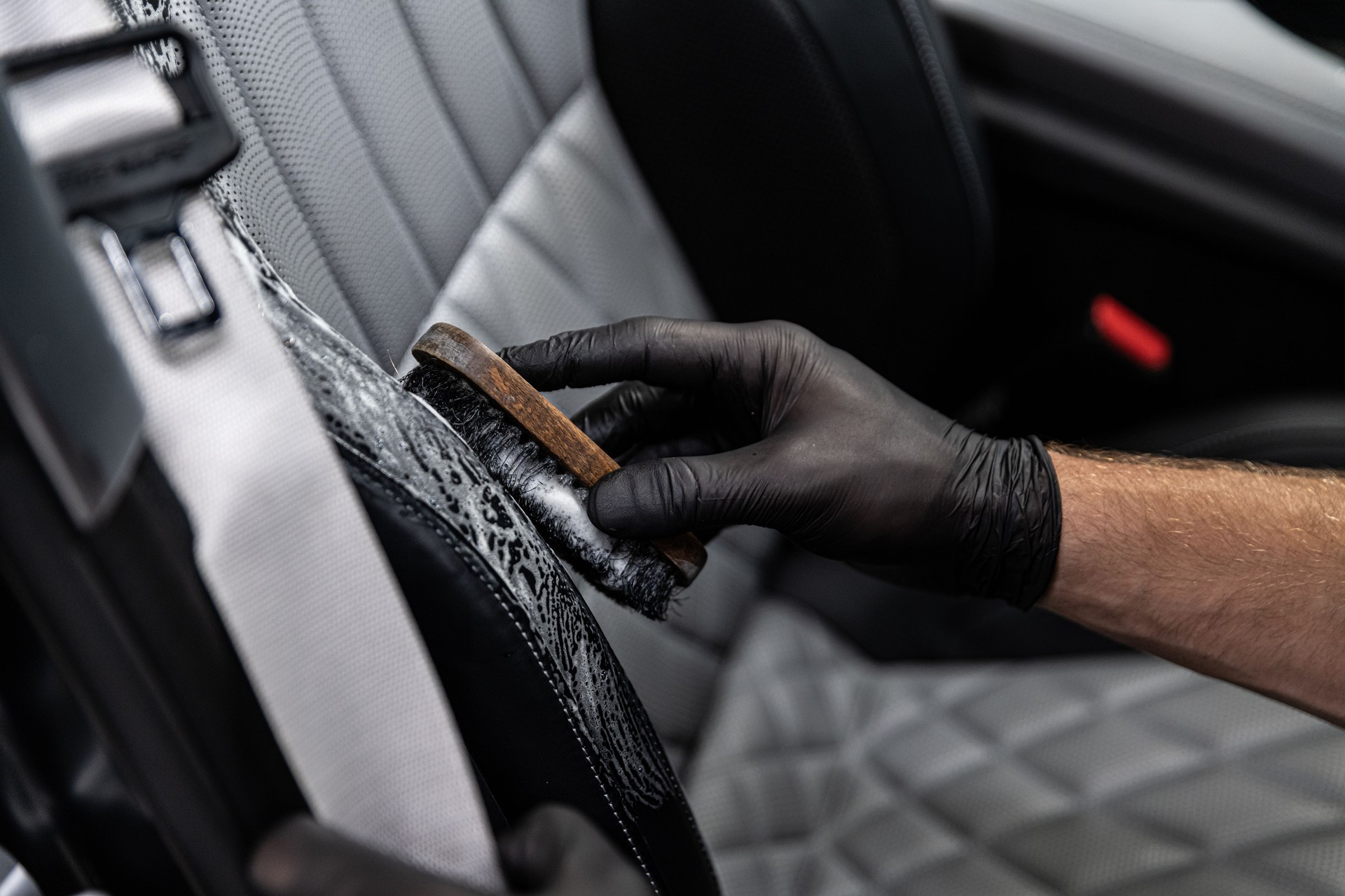 Car detailing studio worker cleaning car interior and car leather seats with a brush.